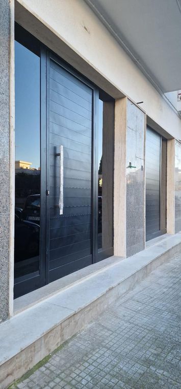Facciata moderna dell'edificio con finestre scure e riflettenti e colonne in pietra lungo un vialetto pavimentato.