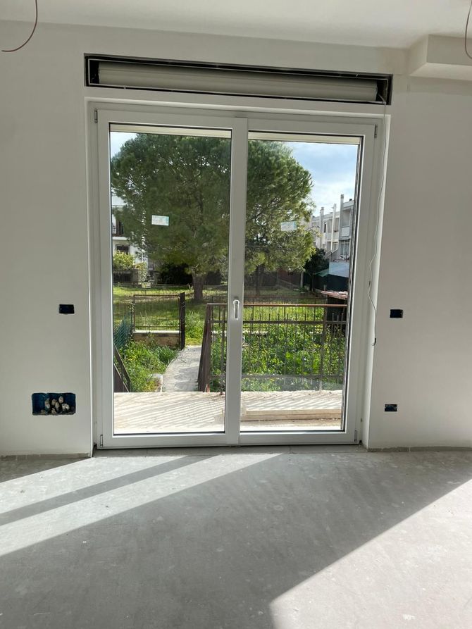 Stanza vuota con porte scorrevoli in vetro che si aprono su un giardino soleggiato e un patio.