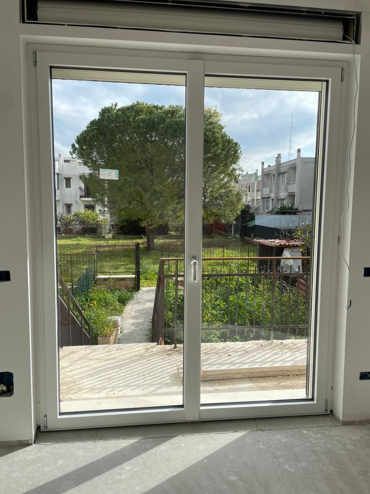 Porte scorrevoli in vetro che si aprono su un soleggiato giardino sul retro con un sentiero e alberi.
