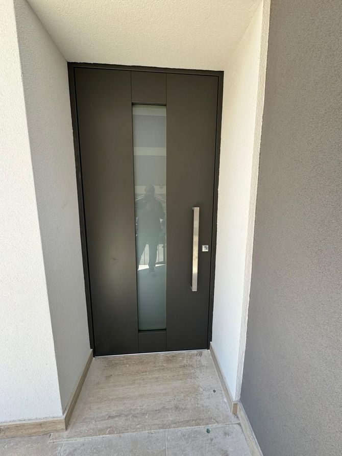 Porta d'ingresso nera con stretto pannello in vetro satinato in una nicchia d'ingresso bianca