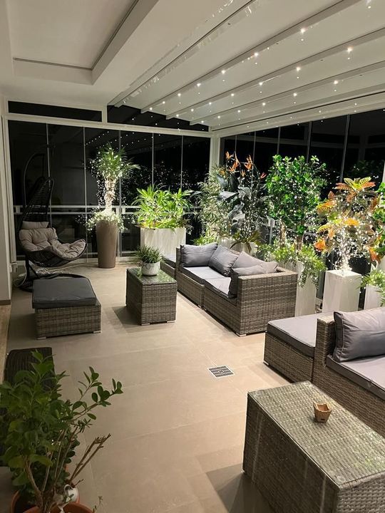 Moderno lounge sul tetto con sedute in vimini, piante in vaso e luci decorative notturne.