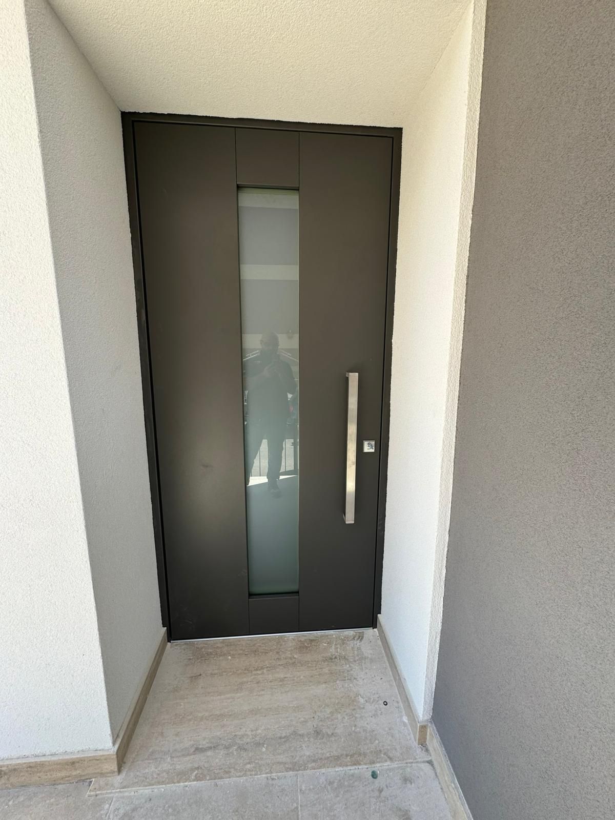 Porta d'ingresso nera con stretto pannello in vetro satinato in una nicchia d'ingresso bianca