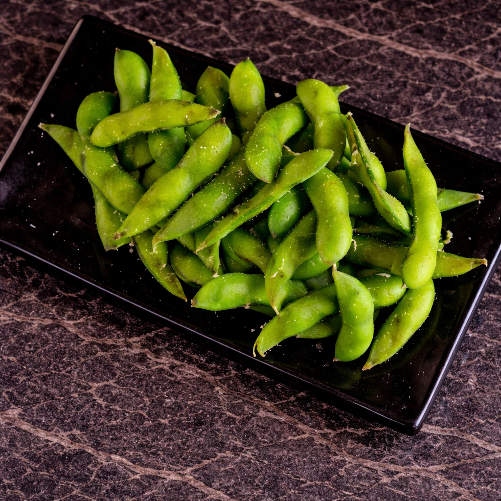 A black rectangular plate filled with steamed, lightly salted green edamame pods on a dark, textured surface.