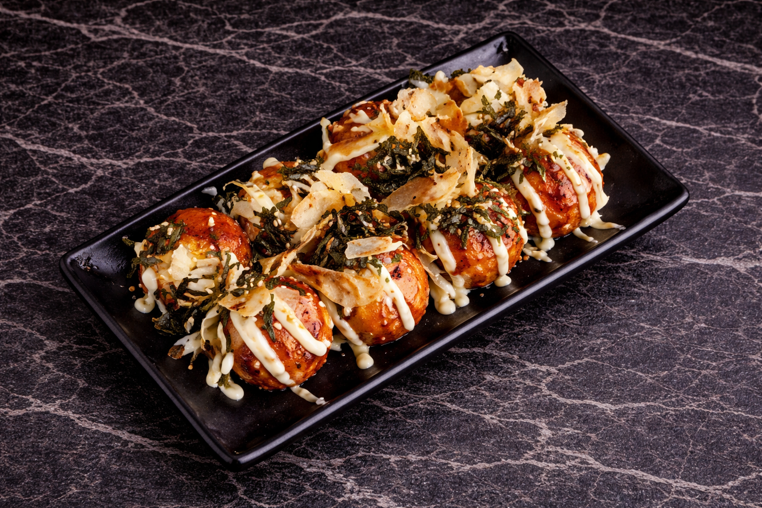 A rectangular plate filled with takoyaki balls topped with drizzles of mayonnaise, seaweed, and bonito flakes.