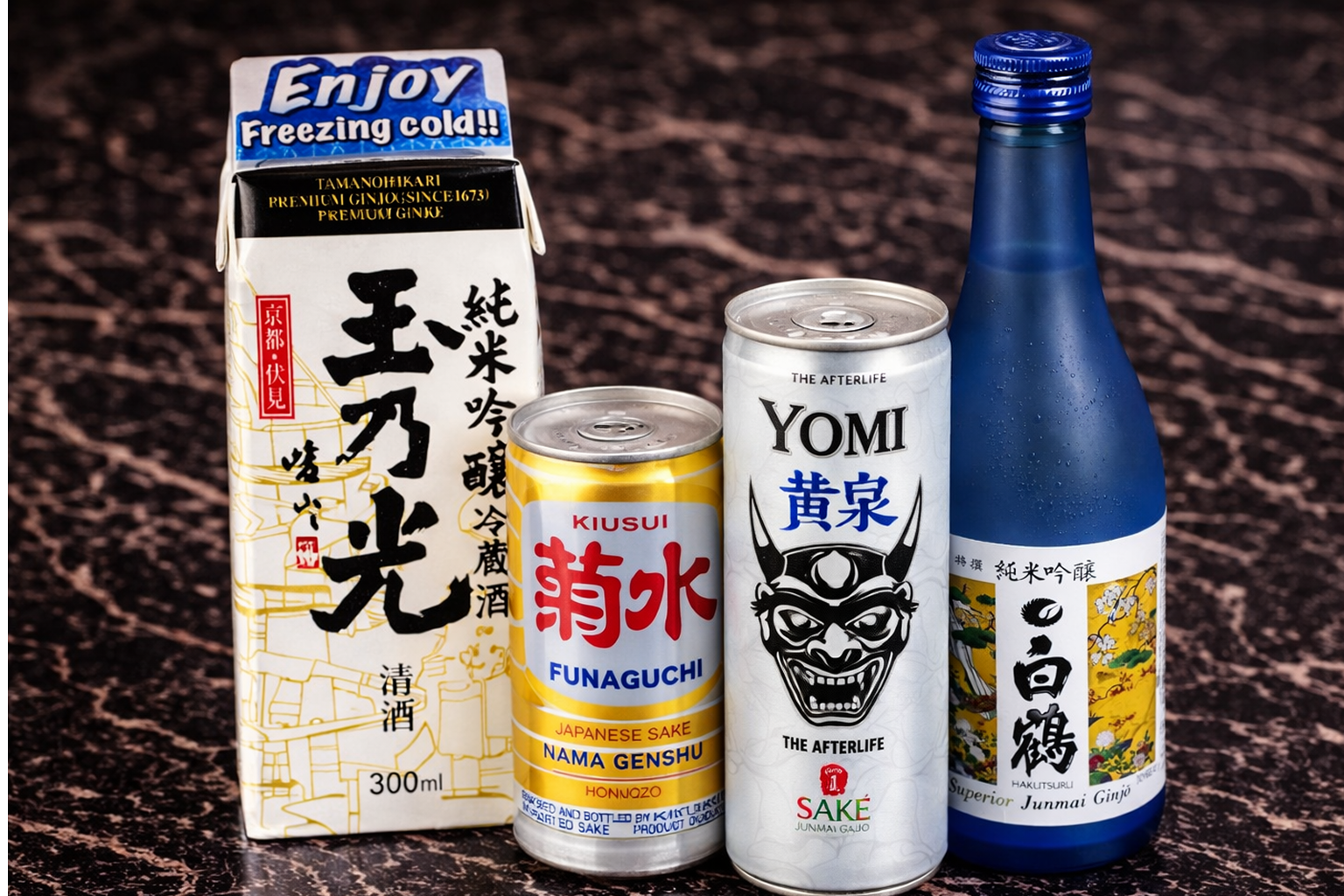 Four Japanese sake containers: a white carton, a gold can, a silver Yomi can, and a blue glass bottle on a dark surface.