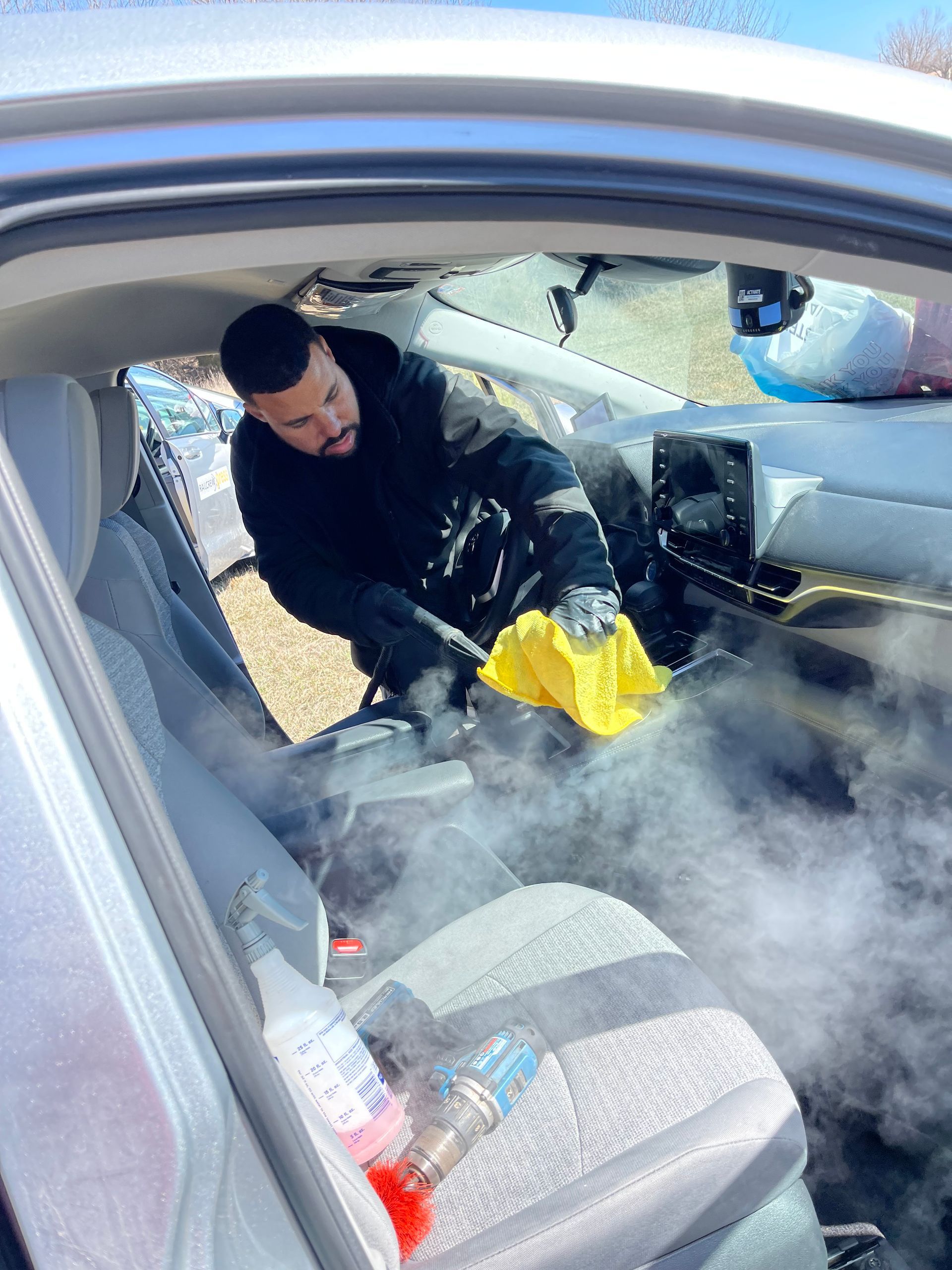A man is cleaning the interior of a car with a steam cleaner.