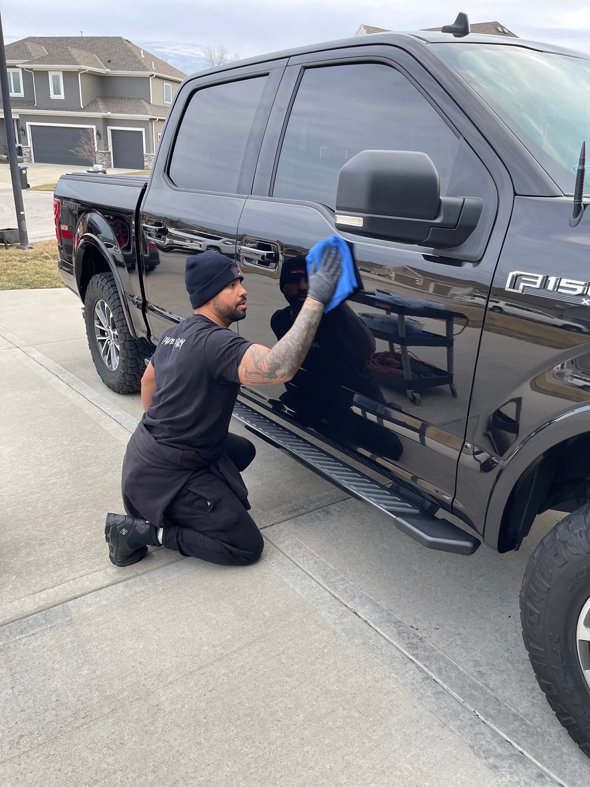 A man is kneeling down to polish a black truck.