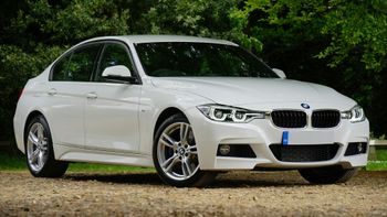 A white bmw 3 series is parked on a gravel road.