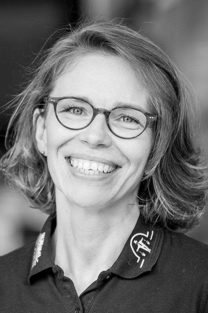 Auf einem Schwarzweißfoto lächelt eine Frau mit Brille und Poloshirt.