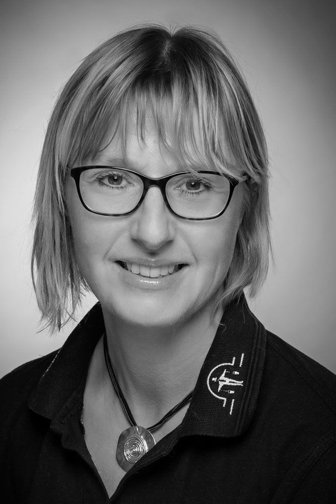 Auf einem Schwarzweißfoto lächelt eine Frau mit Brille und Halskette.