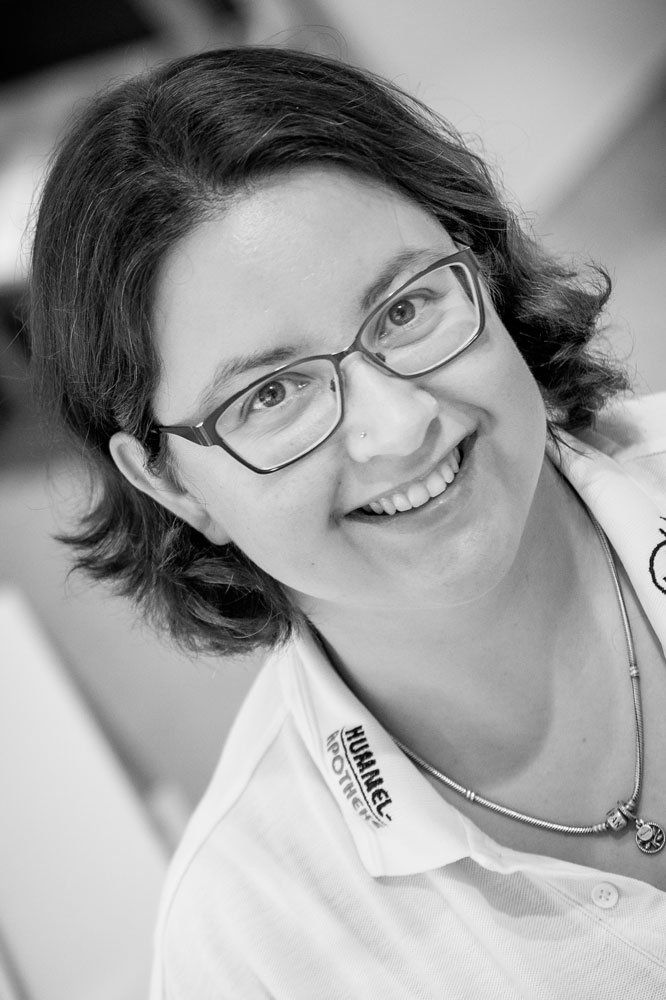 Eine Frau mit Brille und weißem Hemd lächelt auf einem Schwarz-Weiß-Foto.