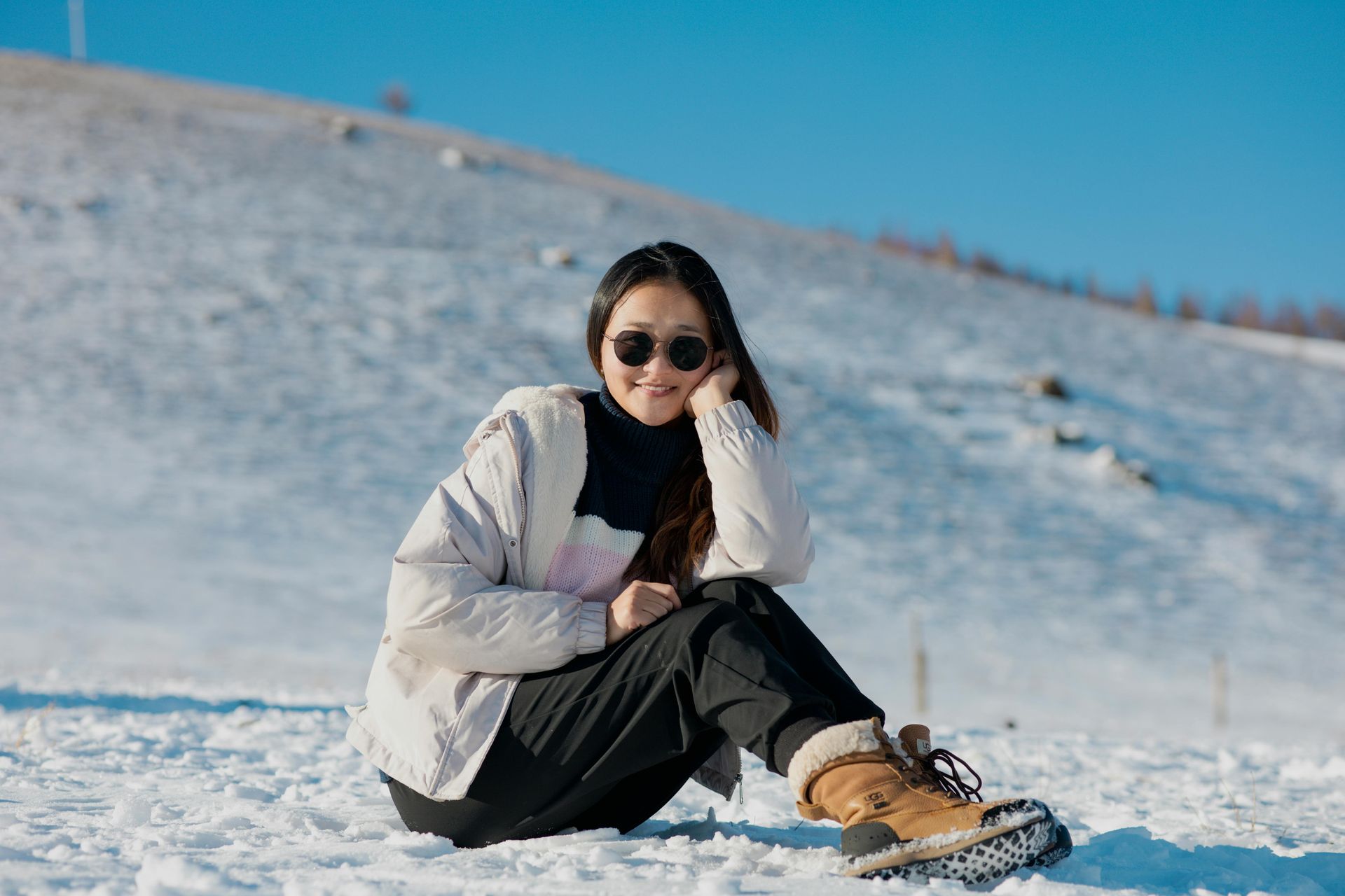 Woman in the winter sitting on the ground with sunglasses on