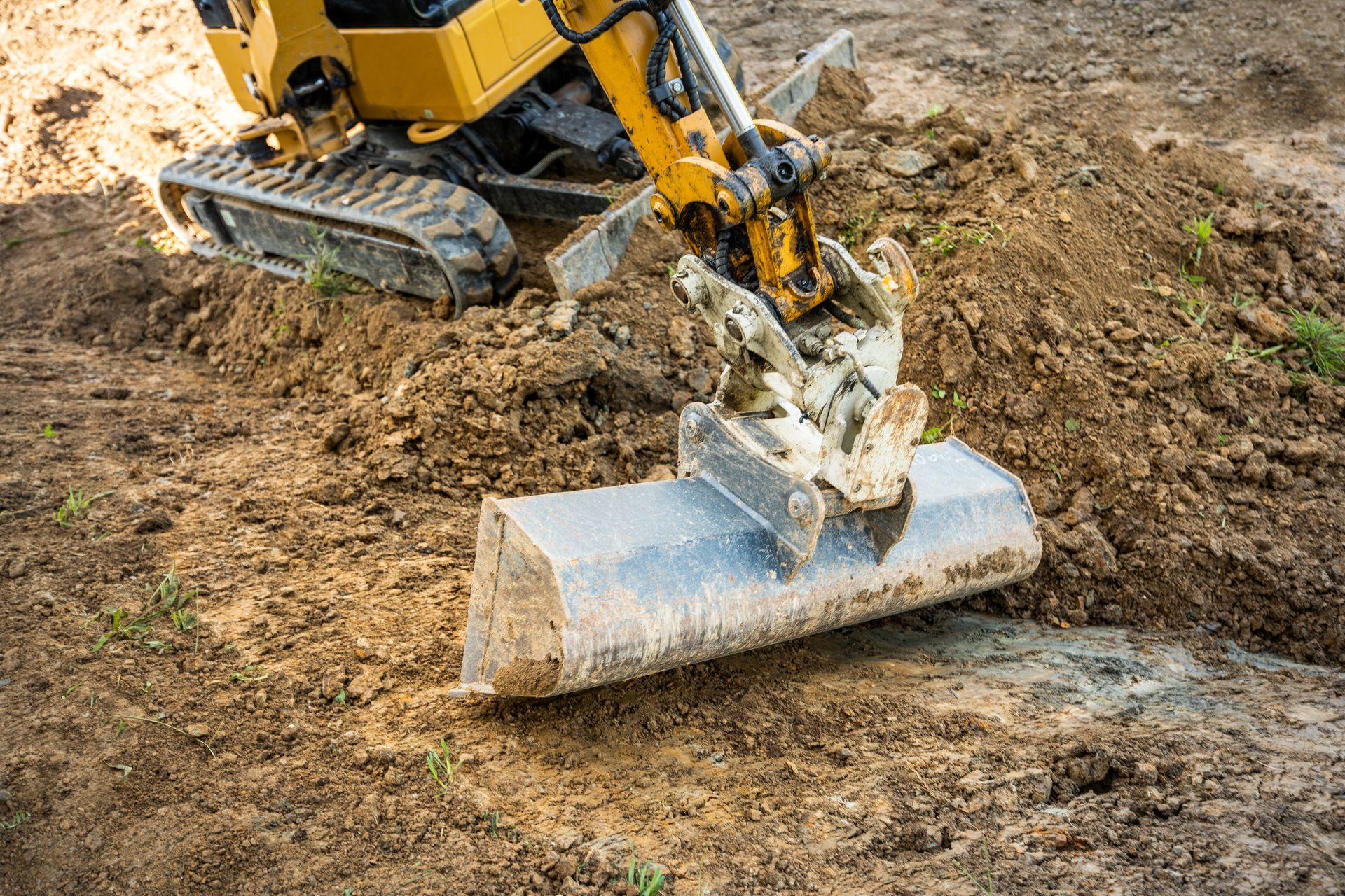 Excavator bucket scraping dirt from a construction site with a concrete block on the ground