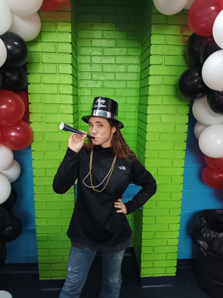 A woman wearing a top hat is blowing a horn in front of balloons.