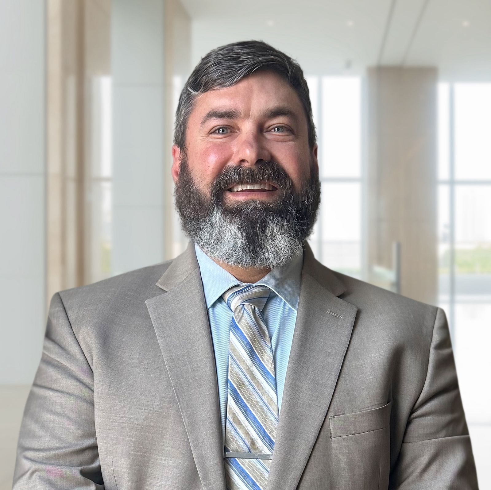 Man in gray suit and tie smiles in office setting.