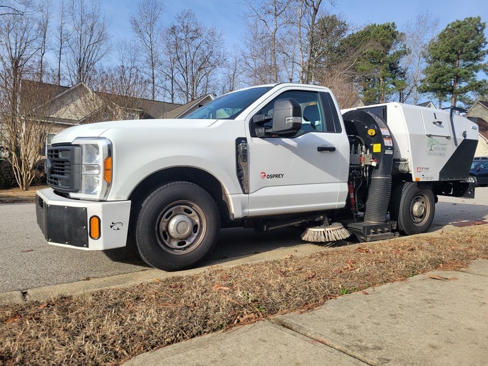 White street sweeper truck parked on a curb in front of houses.