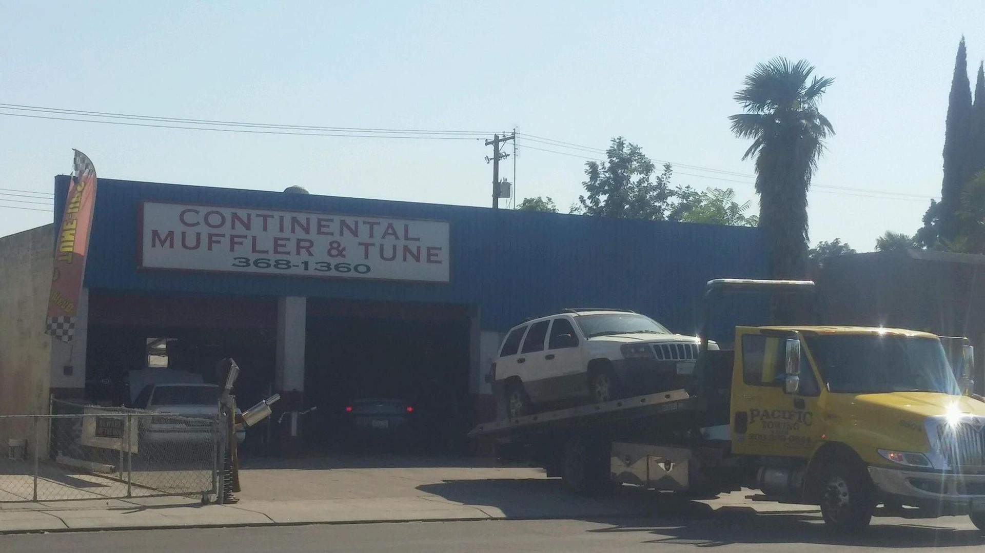 A yellow tow truck is parked in front of continental muffler and tune