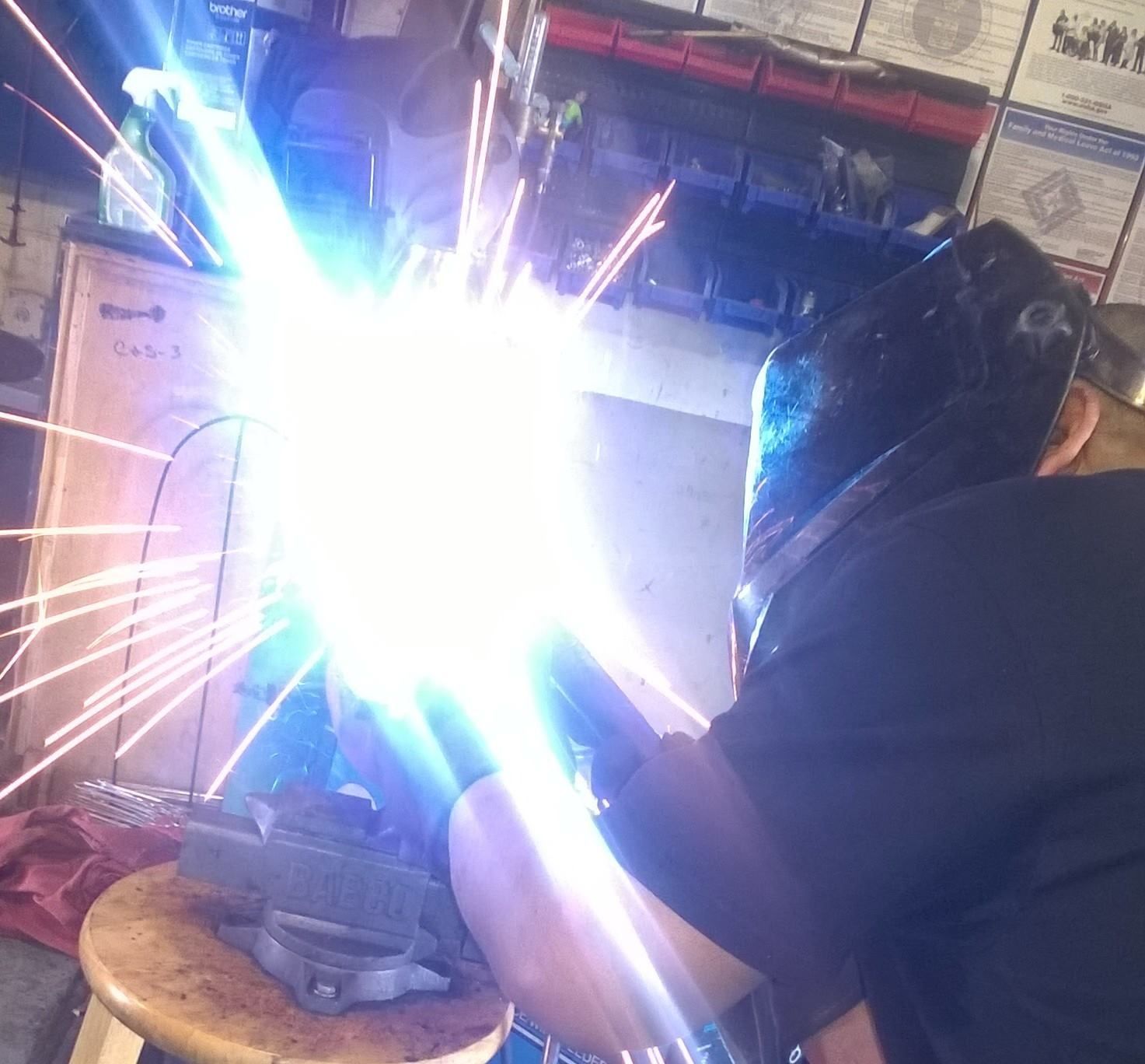 A man wearing a welding mask is welding a piece of metal
