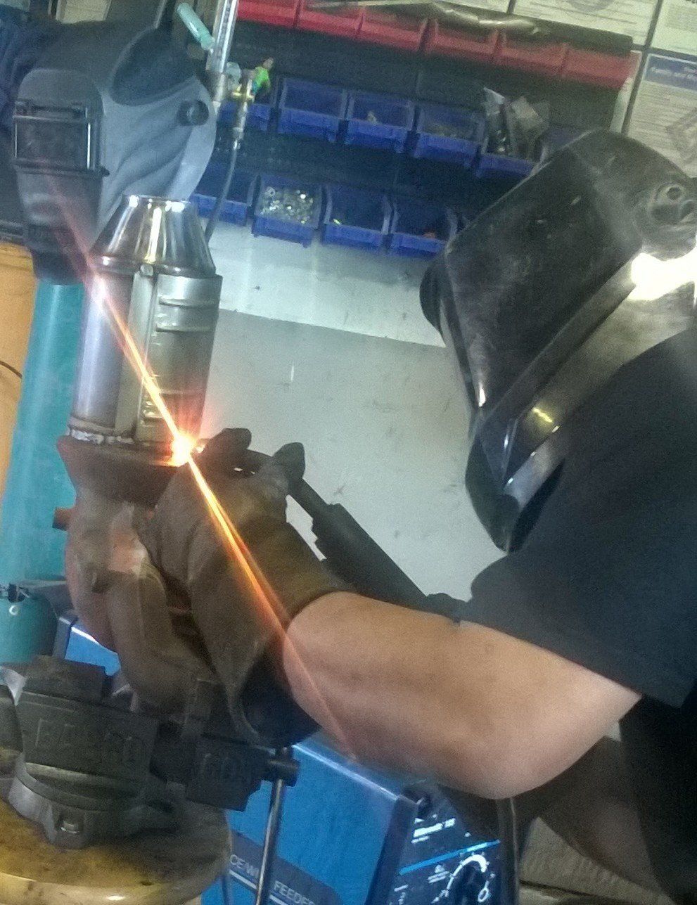 A man wearing a welding helmet is welding a piece of metal