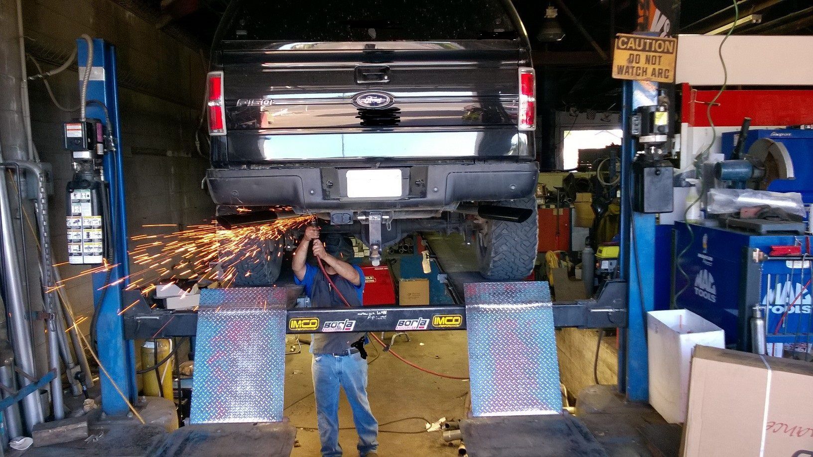 A man is standing in front of a truck on a lift in a garage.