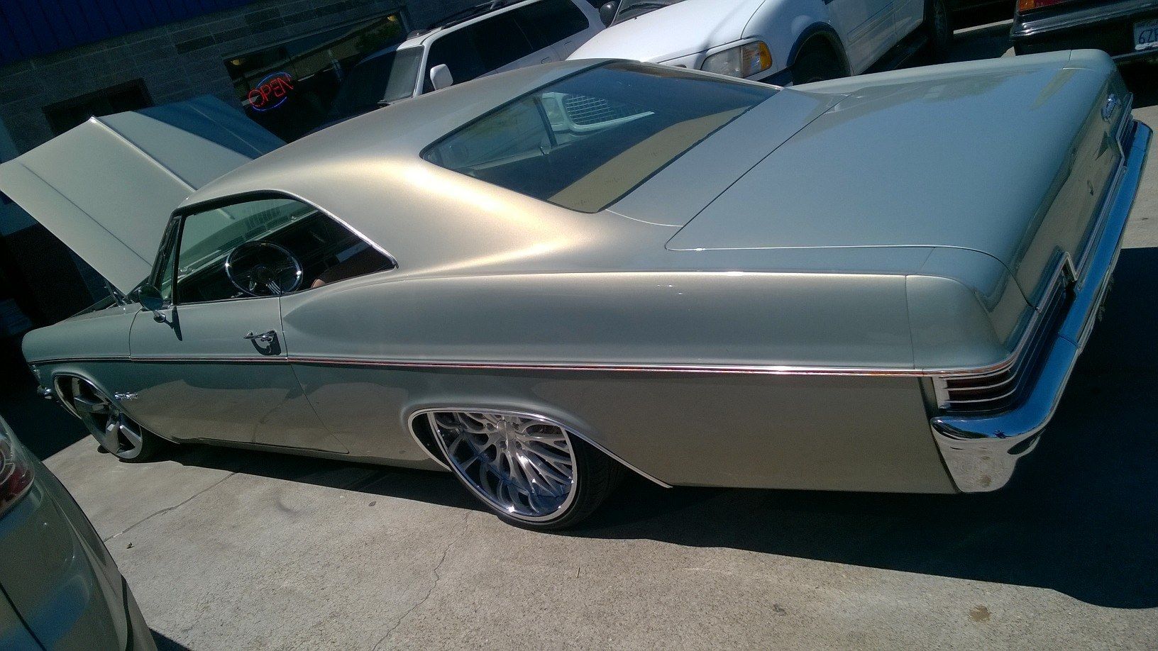 A silver car with the hood up is parked in a parking lot