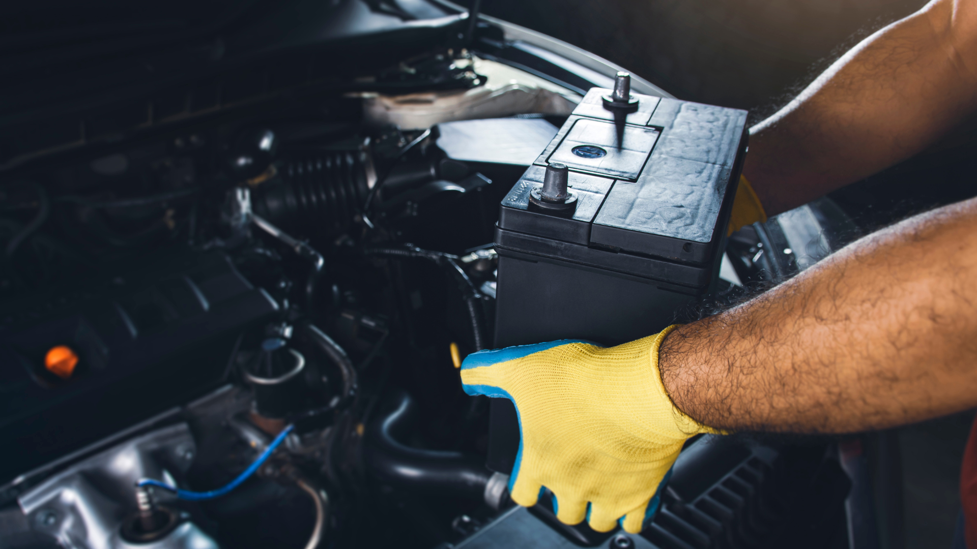 A man wearing yellow gloves is working on a car battery.