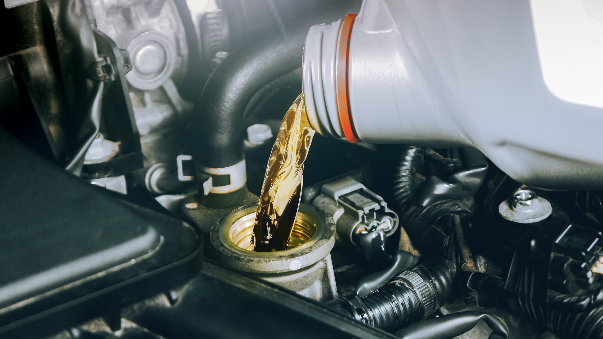 A close up of a person pouring oil into a car engine.