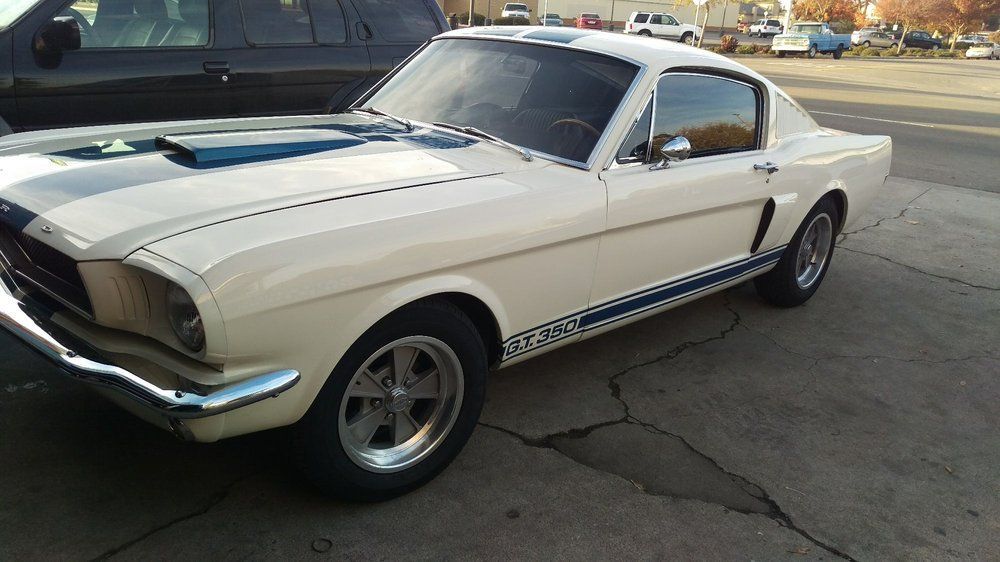 A white mustang is parked in a parking lot next to a black truck.