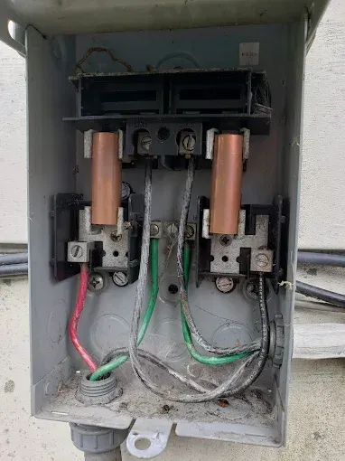 Open electrical box with copper contacts and wiring, including red, black, green, and silver wires, outdoors.