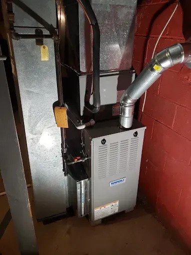 A furnace in a basement setting. The unit is silver and connected to ductwork.