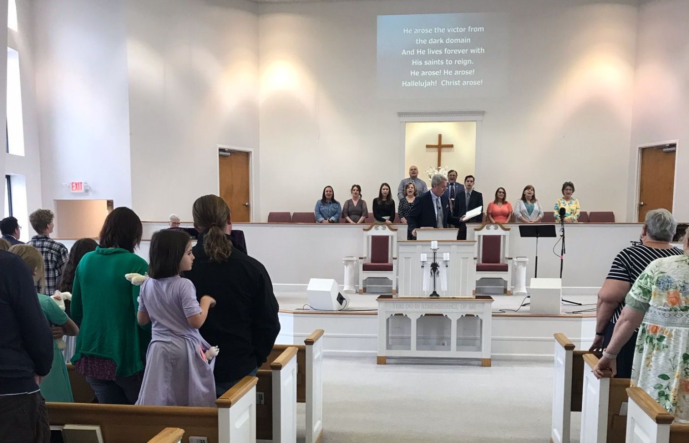 Church service in progress. People standing, singing, and listening to speaker near the altar.