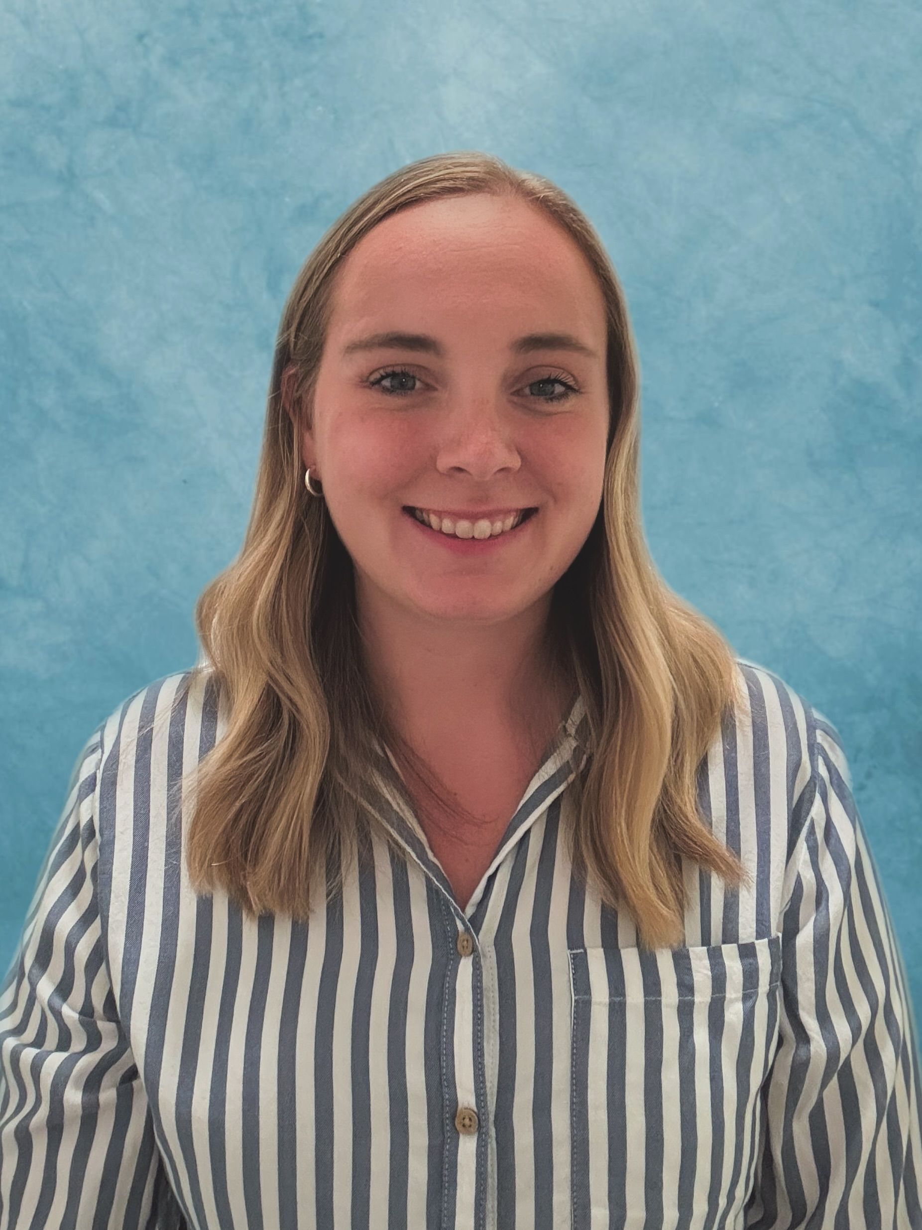 Woman with blonde hair smiles, wearing a blue and white striped shirt against a blue background.