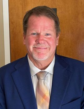 Smiling man in blue suit and tie, indoor setting.