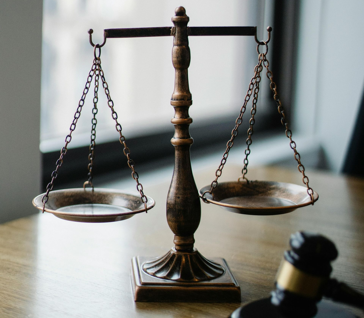 Scales of justice on a wooden table with a gavel; symbolizing law and fairness.