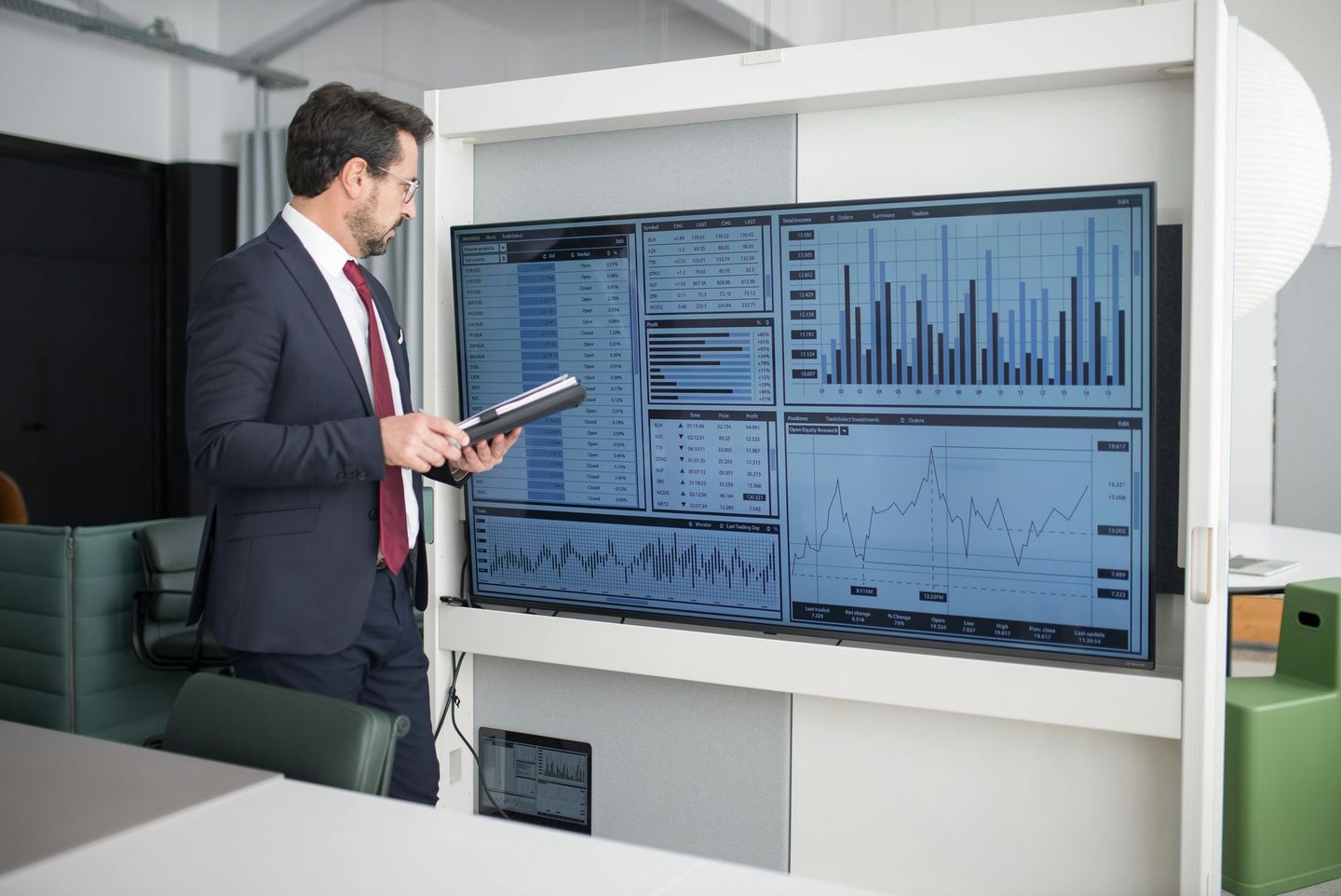 Man in suit looks at data on multiple monitors in office.