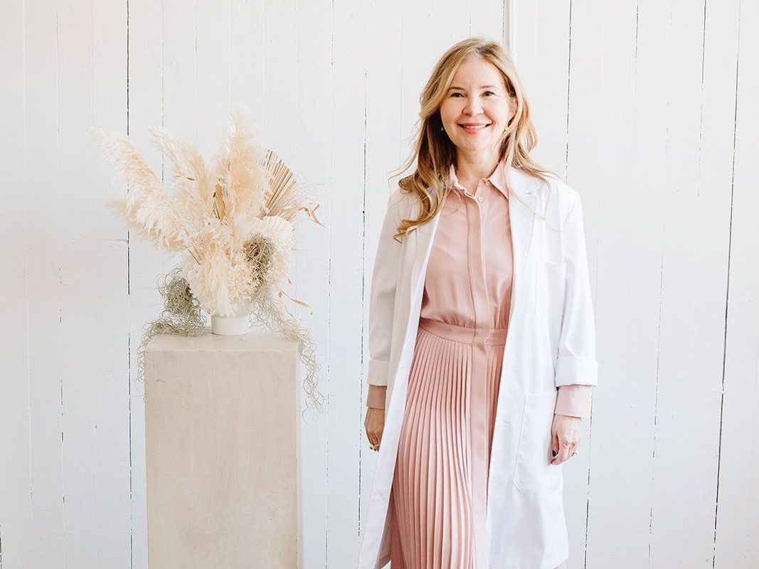 A woman with freckles is smiling with her eyes closed and touching her face.