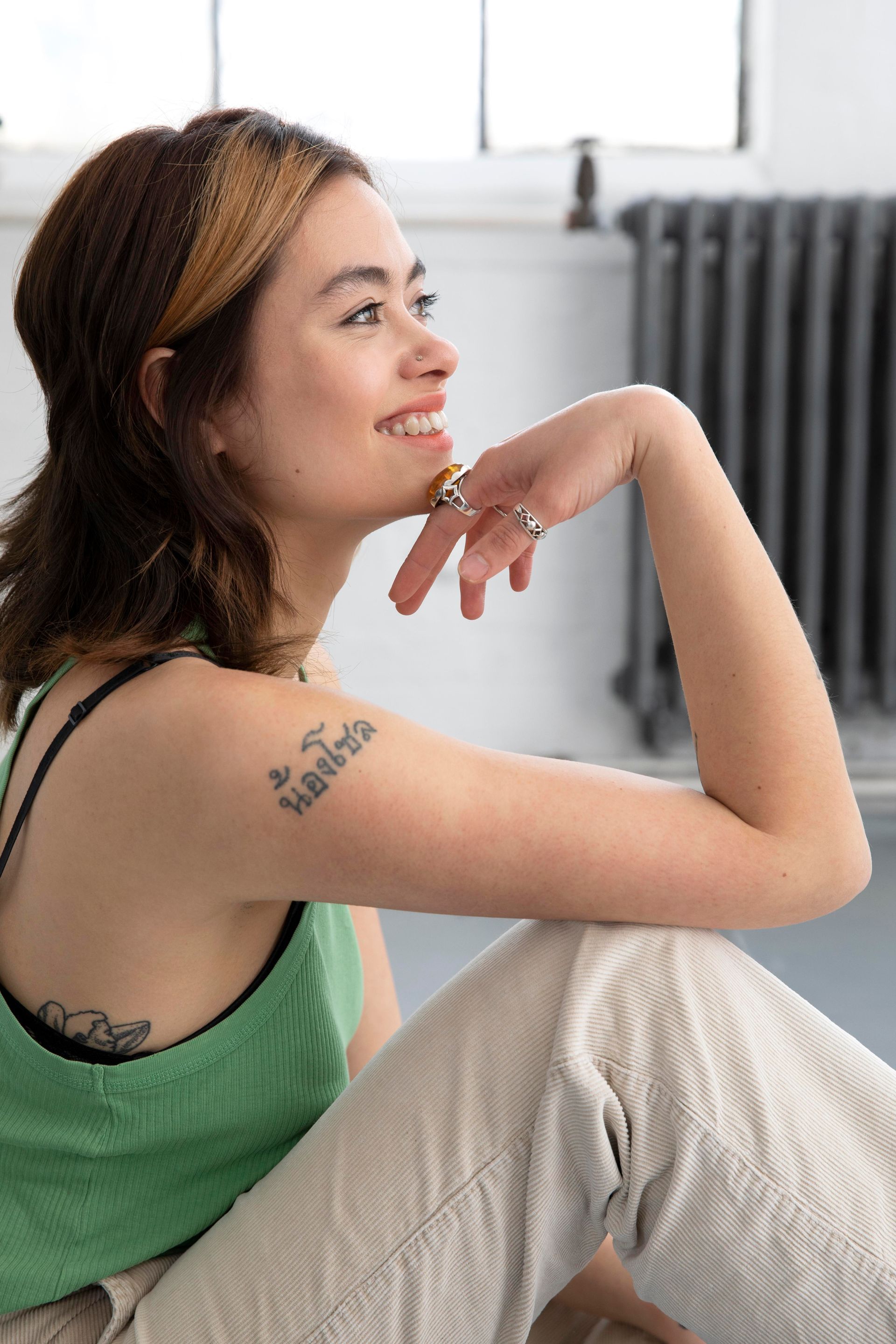 A woman with a tattoo on her arm is sitting on the floor.
