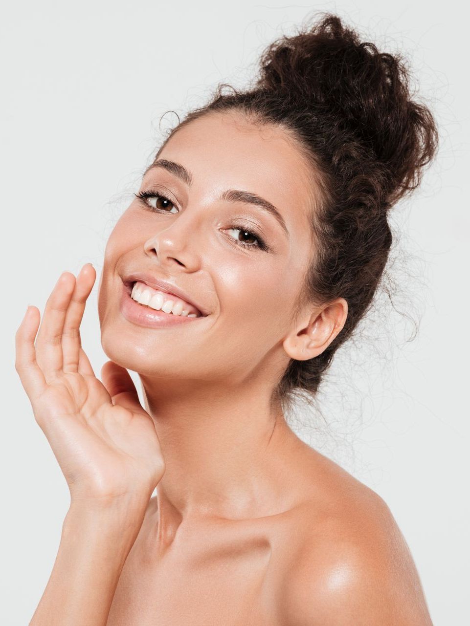 A woman is smiling and touching her face with her hand.
