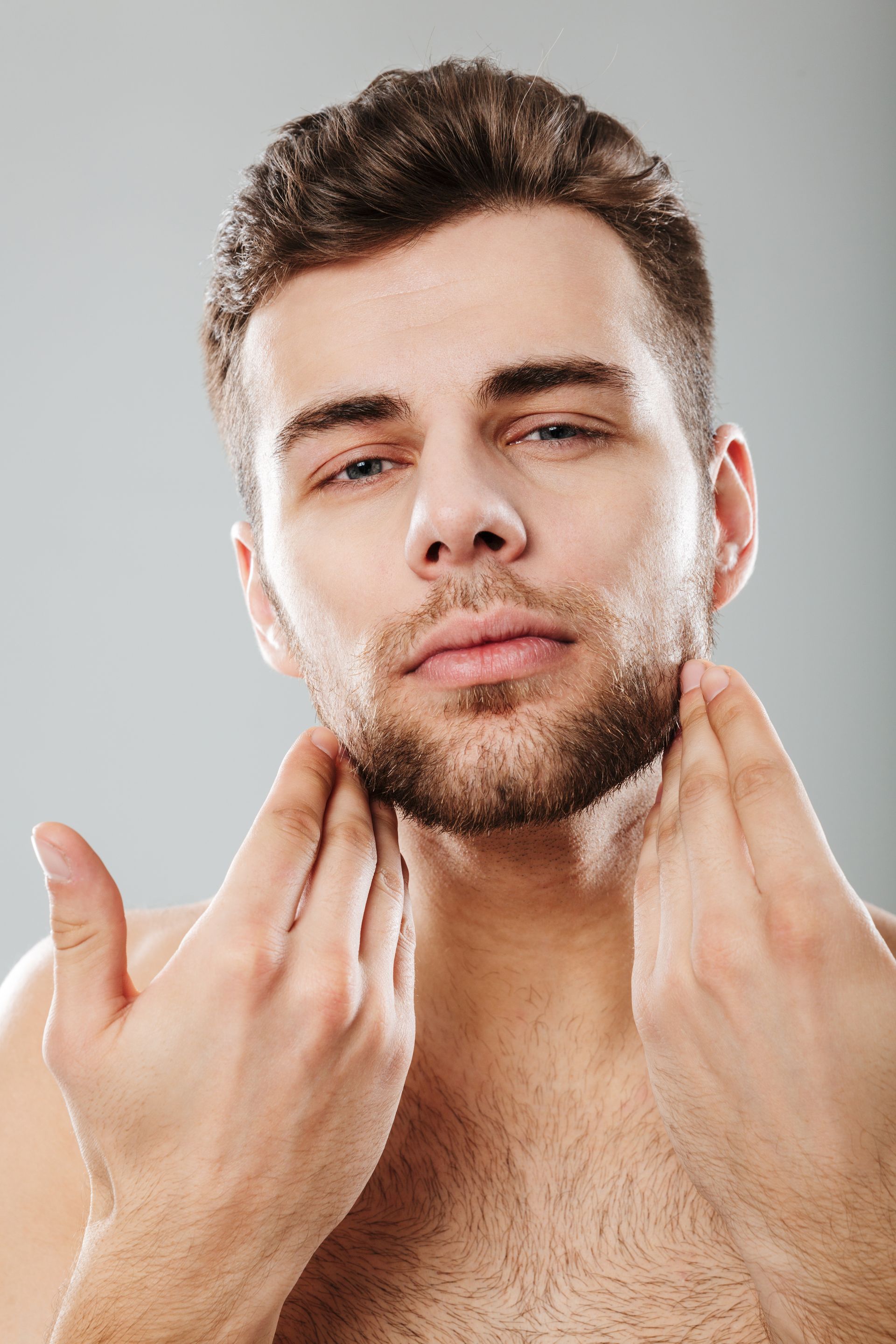 A shirtless man is shaving his beard with his hands.