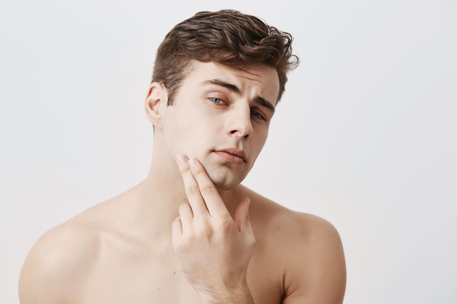 A shirtless man with a beard is looking at his face.