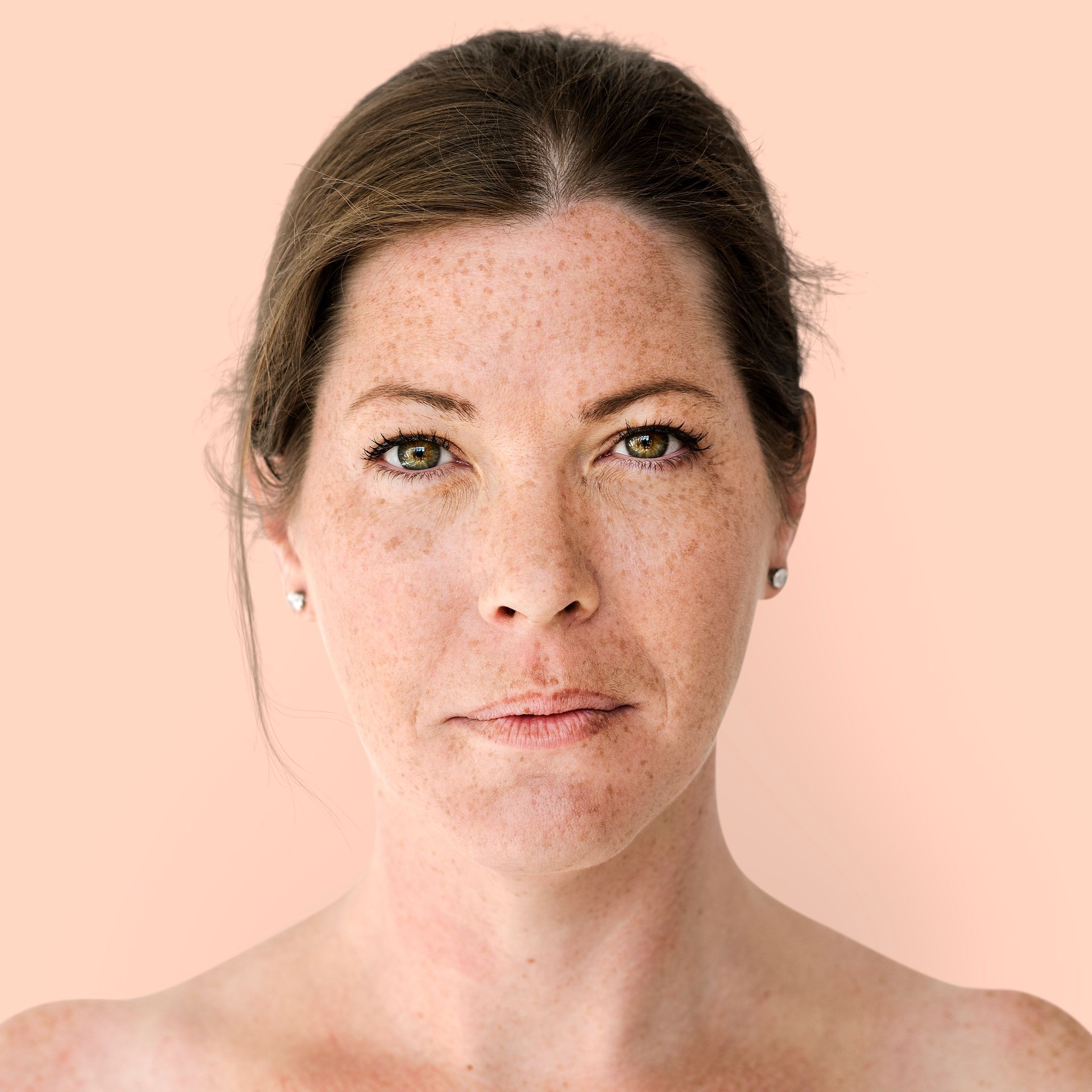 A close up of a woman 's face with freckles against a pink background.