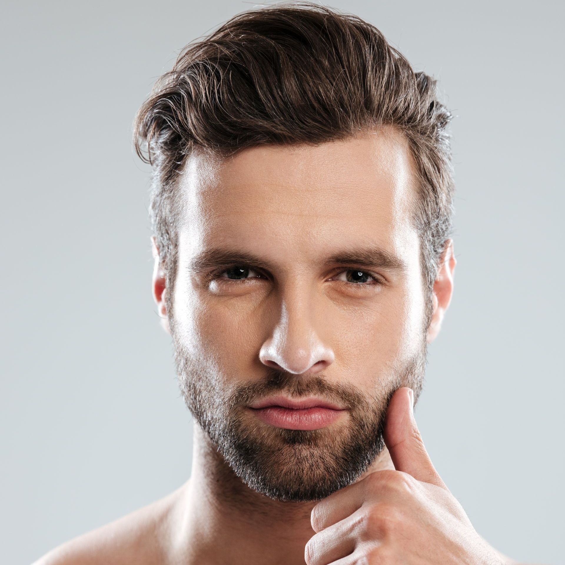 A shirtless man with a beard is holding his hand to his chin.