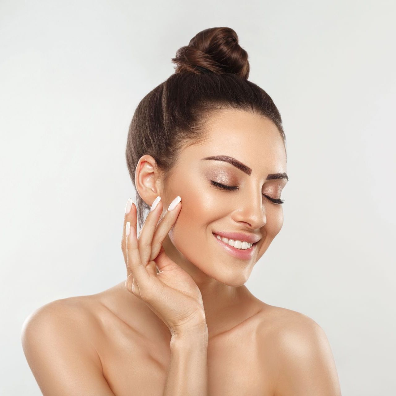 The woman is smiling and touching her face with her hand.