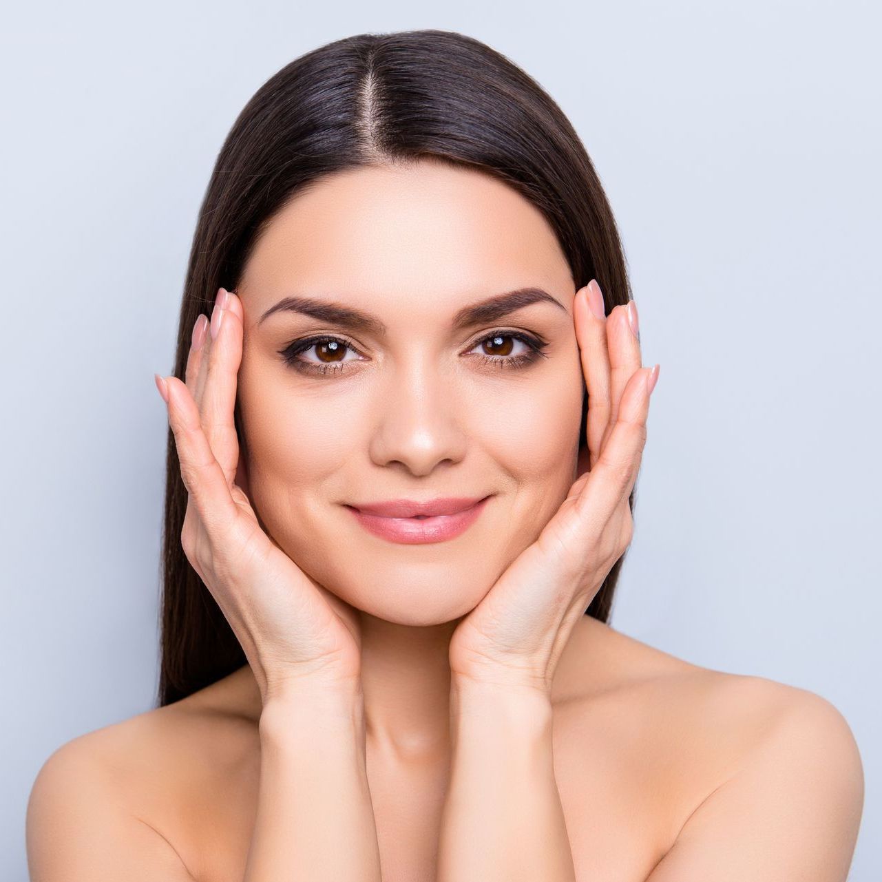 A woman is touching her face with her hands and smiling.