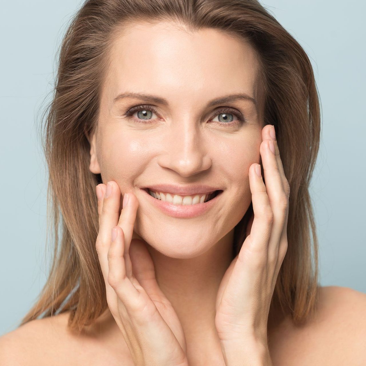 A woman is smiling and touching her face with her hands.