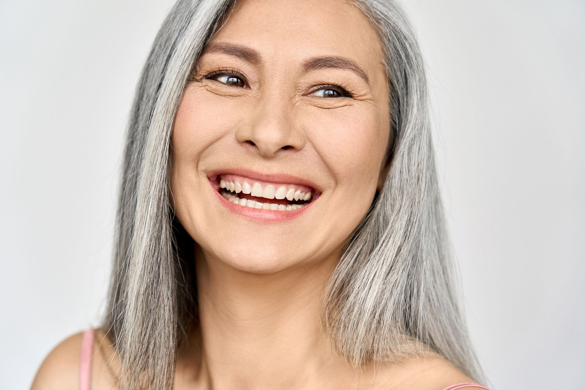 A person with long, gray hair smiling warmly against a plain, light-colored background.