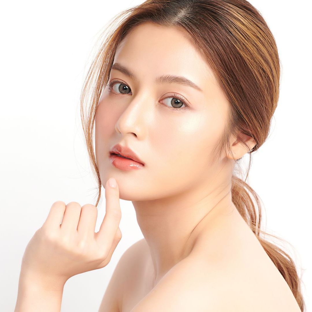 A woman is touching her face with her finger and looking at the camera.