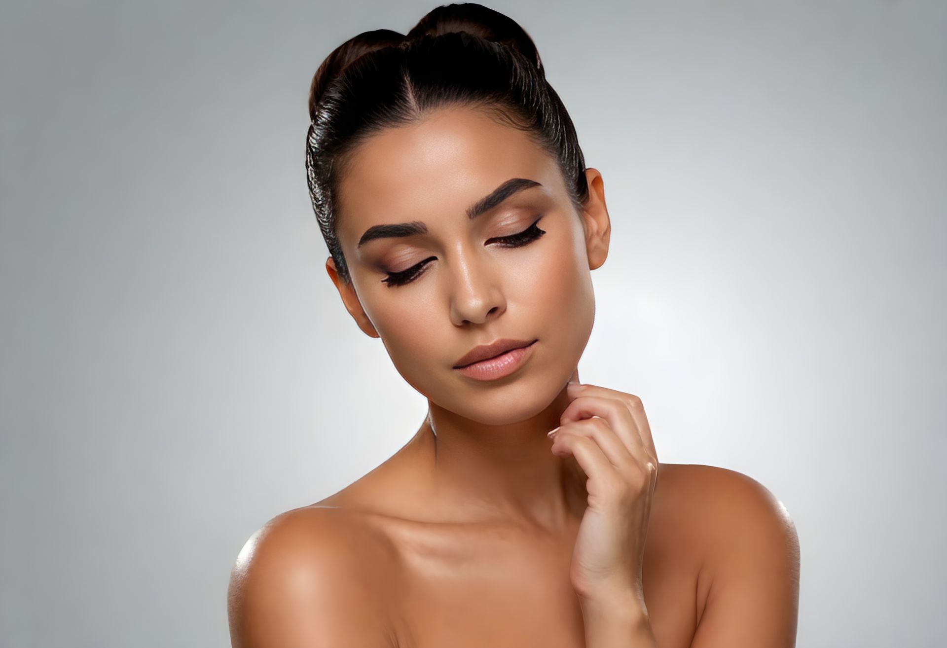 Woman with closed eyes, hand near neck, updo hairstyle, against a light gray background.
