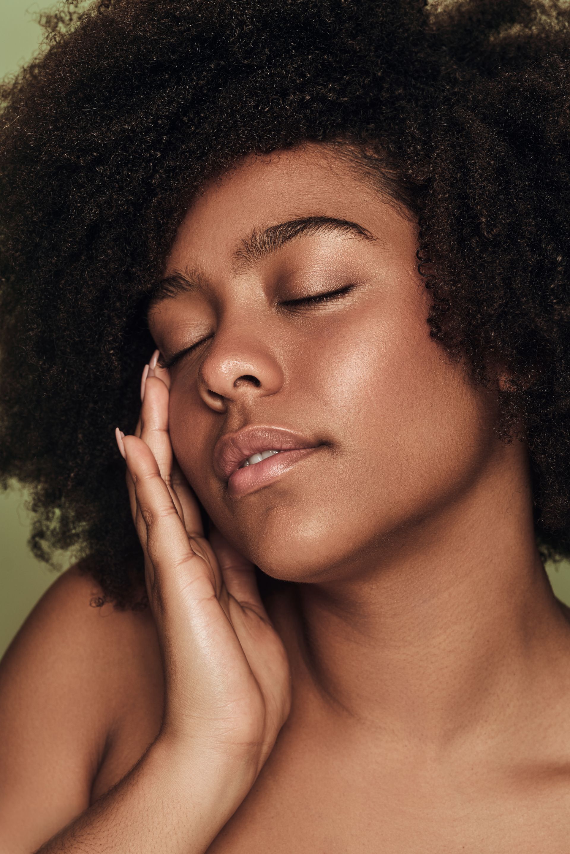 A close up of a woman 's face with her eyes closed and her hand on her face.