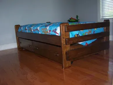A wooden bed with drawers underneath it in a bedroom.
